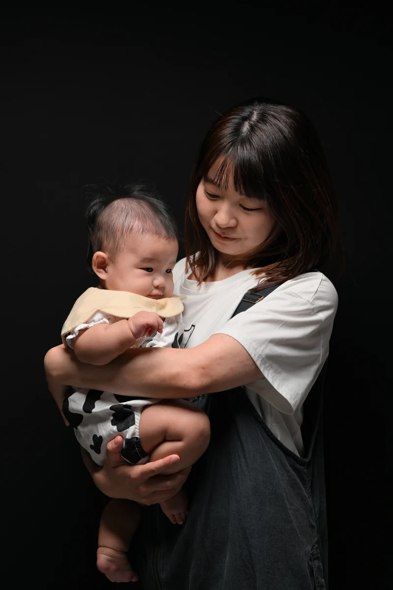 黒背景で赤ちゃんを抱き、顔を見つめる母親のポートレート