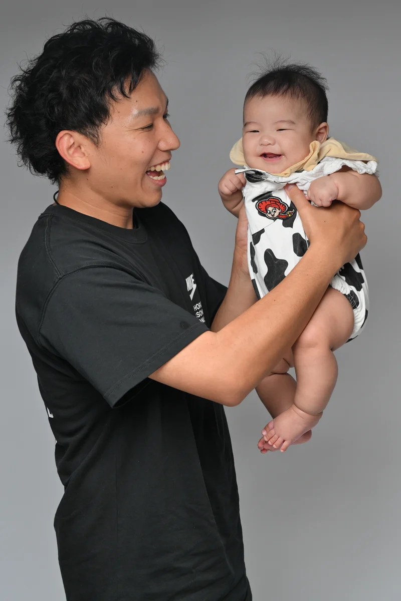 グレーの背景で笑顔の赤ちゃんを抱き上げる父親
